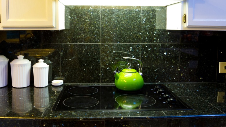Green tea pot and white porcelain jars sitting on green granite countertop with matching backsplash in kitchen