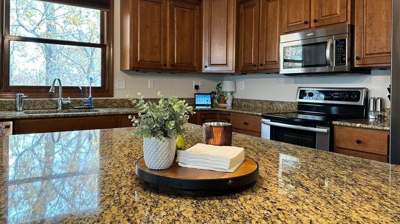Kitchen with dark wood cabinets and gold toned granite counter displaying wooden stand with potted plant and napkins