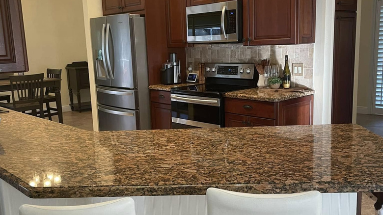Kitchen with brown granite counters, dark cherrywood cabinets, steel appliances, and white counter chairs
