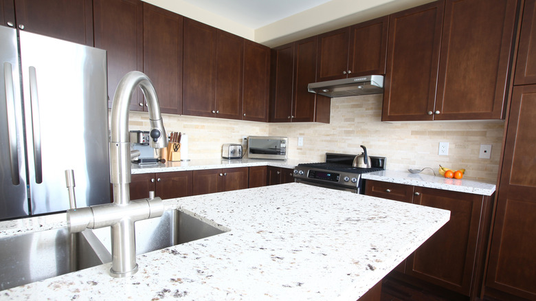 A kitchen with a white quartz countertop and brown wooden cupboards.