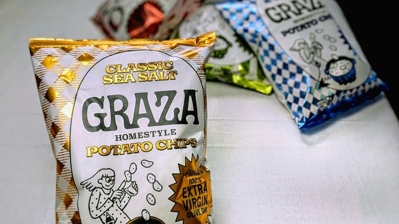 A close-up of Graza's sea salt potato chips with three other chip bags blurred in the background