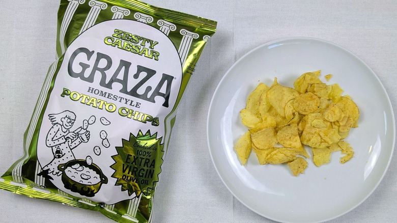 A bag of Graza Zesty Caesar potato chips and a white plate of chips on a white tablecloth