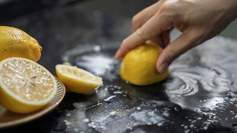 A person scrubbing a glass stove top with a half lemon