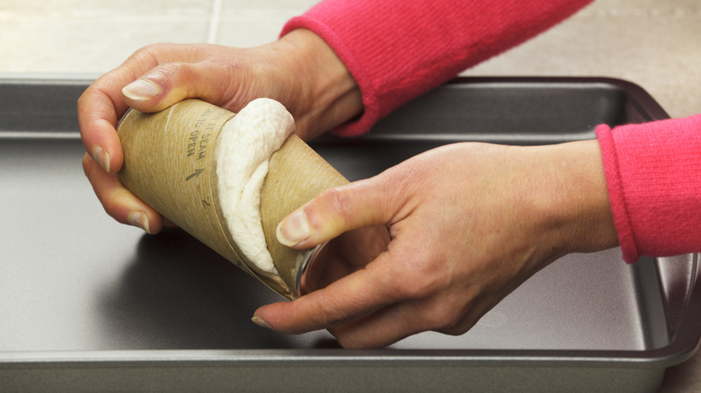 person holding a premade biscuit dough in a cardboard tube
