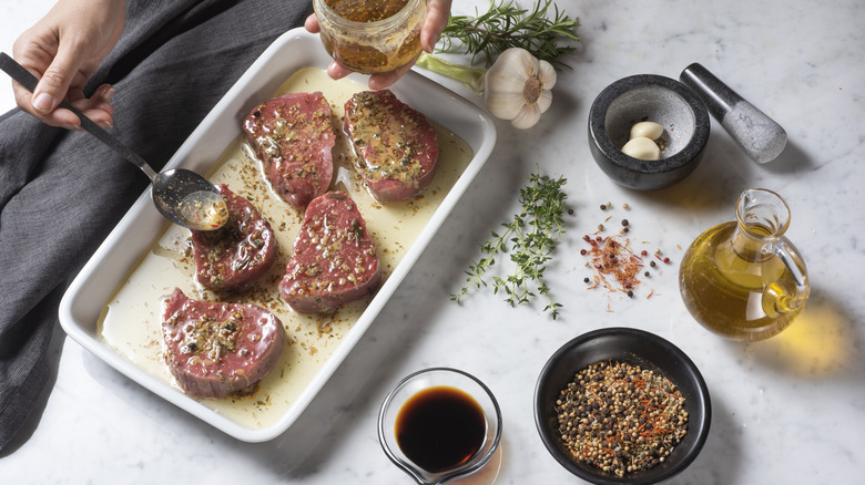 Person spreading marinade on steaks