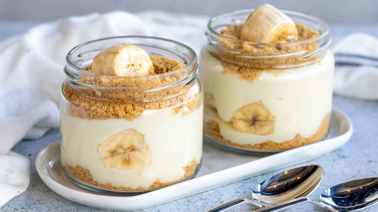 Two jars of banana pudding topped with granola dust and sliced bananas