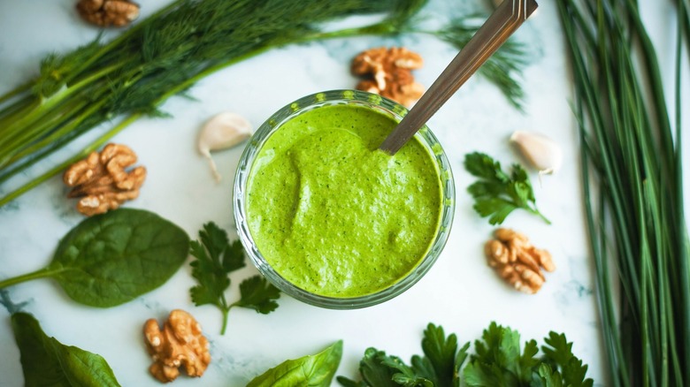 Green goddess dressing in a bowl surrounded by herbs