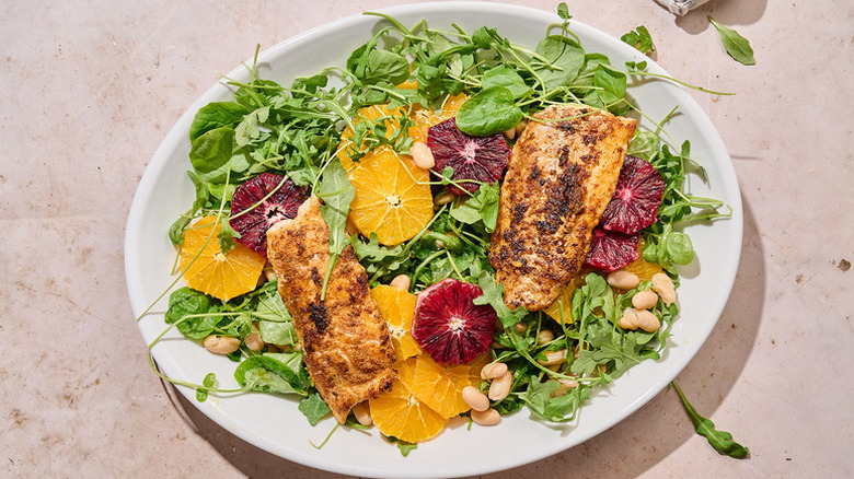 Leafy green salad with cod and orange on white serving plate