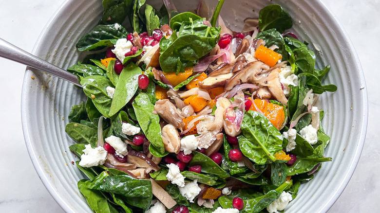 Bowl of spinach and mushroom salad with crumbled feta and pomegranate seeds