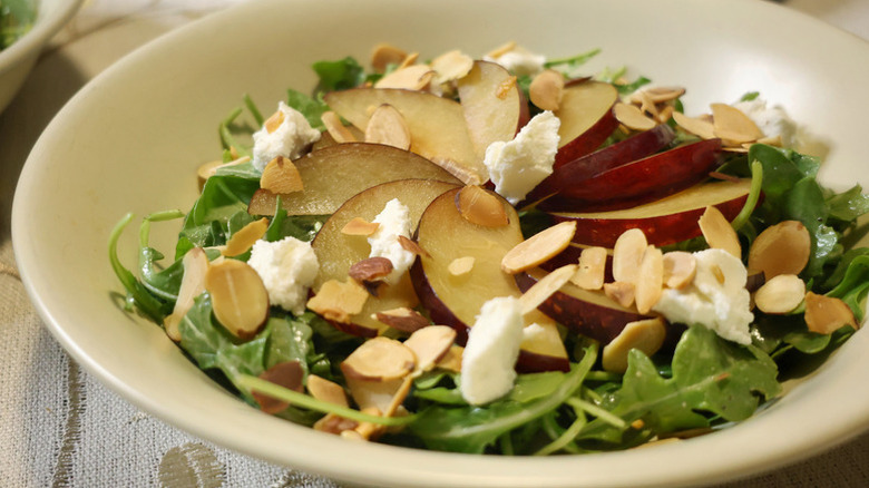 Bowl of arugula, plum, and chèvre salad with slivered almonds