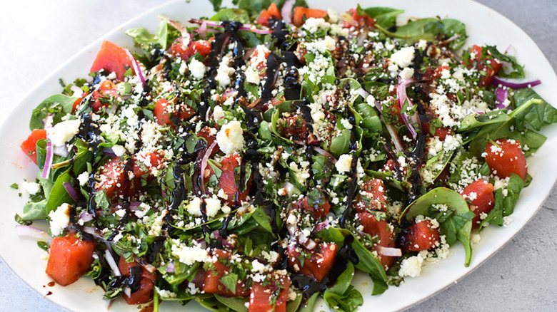 Watermelon, spinach, and feta salad on serving platter, drizzled with balsamic dressing