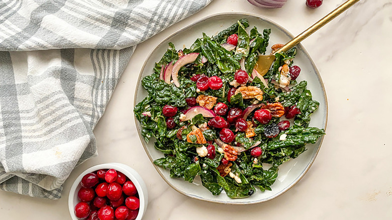 Plate of kale, cranberry, and walnut salad next to bowl of cranberries