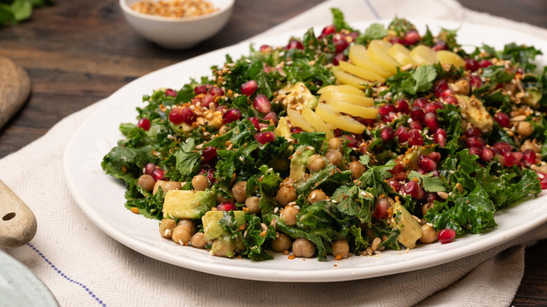 Kale, chickpea, and dukkah salad with pomegranate seeds on white serving plate