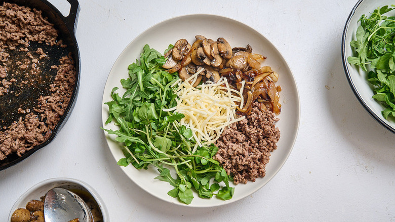Arugula salad bowl with sauteed mushrooms, shredded cheese, and ground beef
