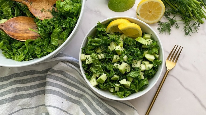 Mustard green and green apple salad serving into white bowl with lemon wedges