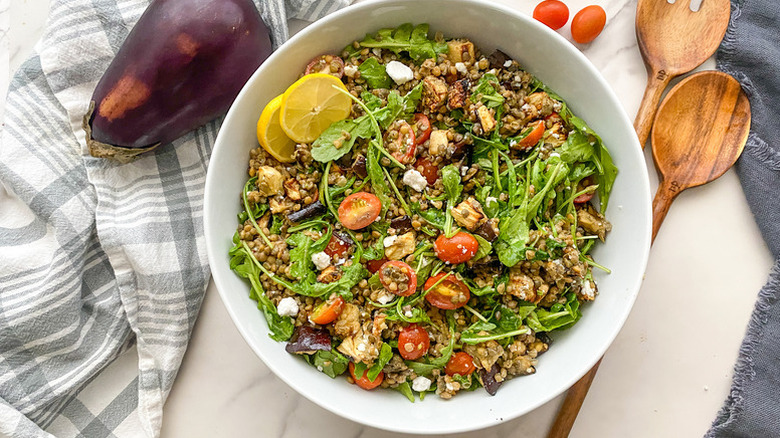 Roasted eggplant, arugula, and lentil salad in white bowl with lemon slices