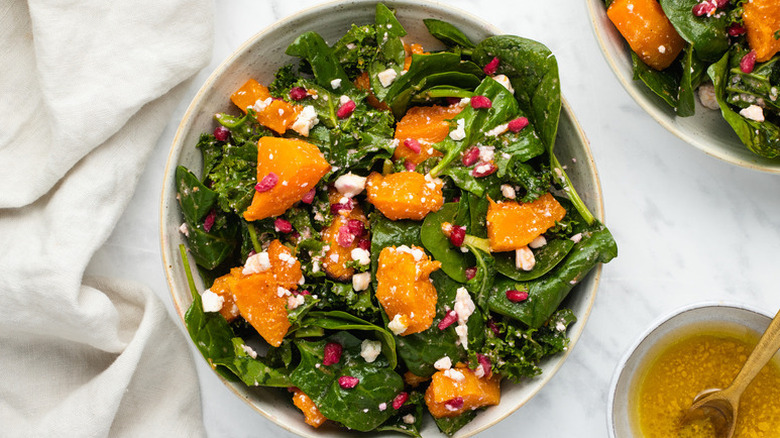 Bowl of spinach salad with roasted butternut squash, crumbled feta, and pomegranate seeds