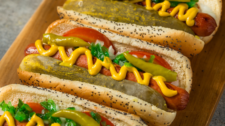 Three Chicago-style hot dogs on a wooden board