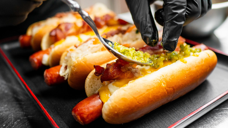 A closeup of person's gloved hand topping a hot dog