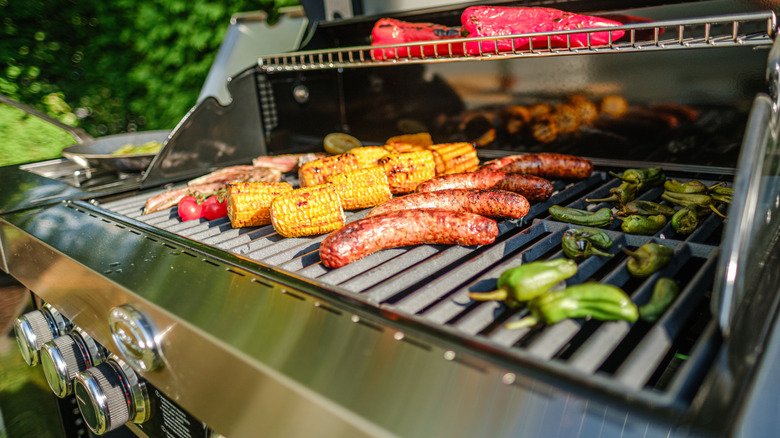 Sausages, corn on the cob, and peppers cooking on an outdoor gas grill