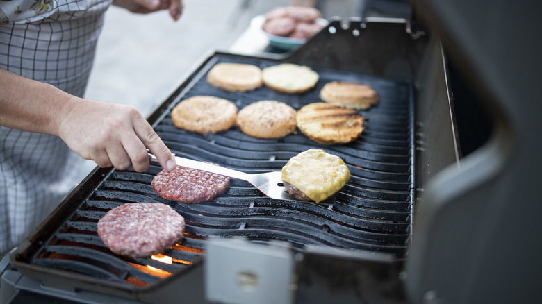 Person grilling burger patty and toasting buns