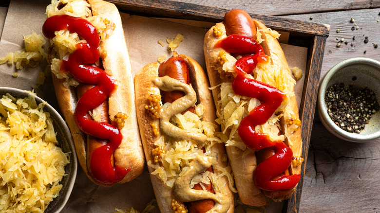 Bratwurst sausages on buns dressed with ketchup, mustard, sauerkraut, and more
