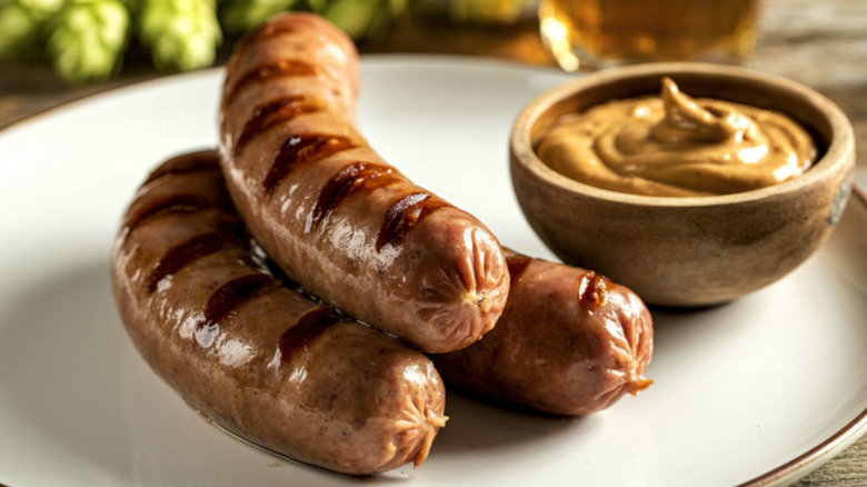 Grilled bratwurst sausage on a plate with mustard and beer in the background
