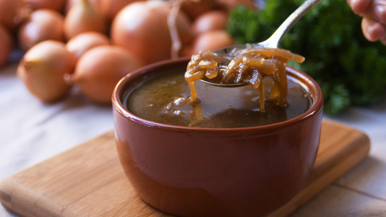A spoon pulling a scoop of French onion soup out of a bowl