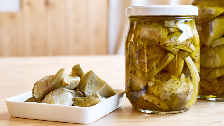 Small dish of artichoke hearts beside two jars of the same