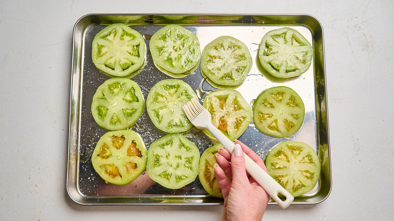 brushing tomatoes with oil on a sheet tray