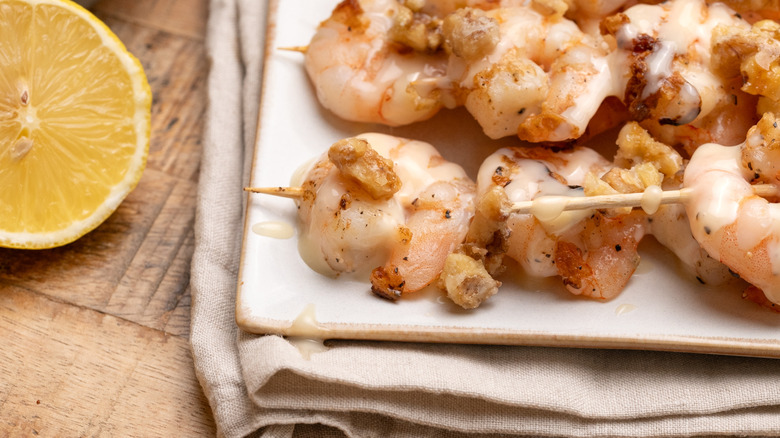 close up of grilled honey walnut shrimp skewers on plate next to halved lemon on table