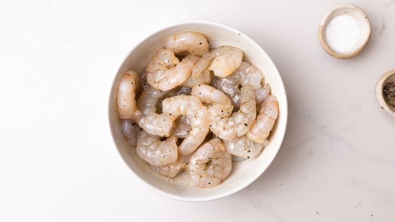 seasoned raw shrimp in bowl next to small dishes of salt and pepper