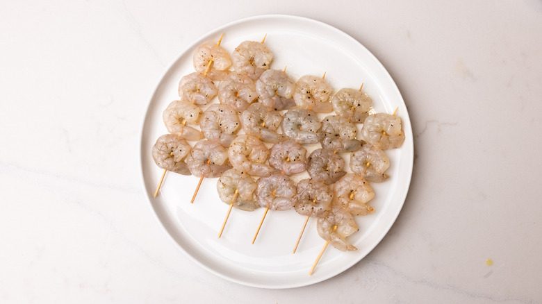 seasoned raw shrimp on wooden skewers laid out on plate