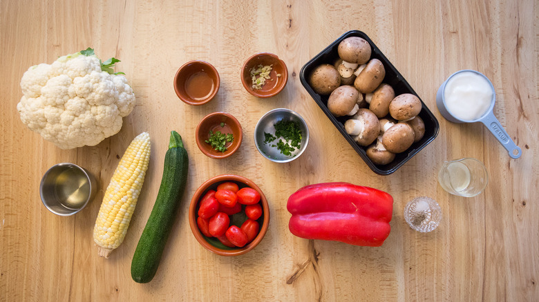 cauliflower, corn, zuchinni, tomatoes, red pepper, cremini mushrooms, and other veggie skewer ingredients on table