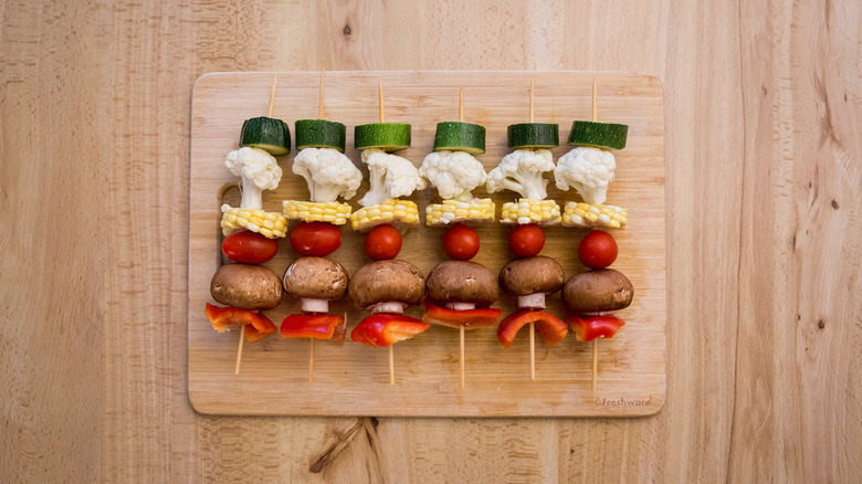 uncooked veggie skewers lined up on wooden cutting board