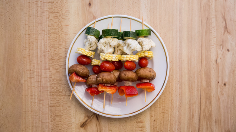 uncooked veggie skewers piled on white plate