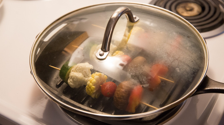 veggie skewers cooking in pan with lid on top on the stove