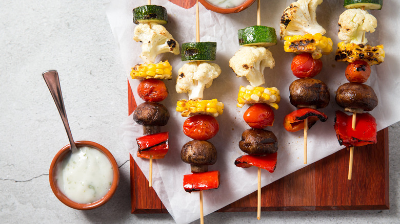 Close up of veggie skewers served on wooden board lined with parchment paper next to yogurt sauce