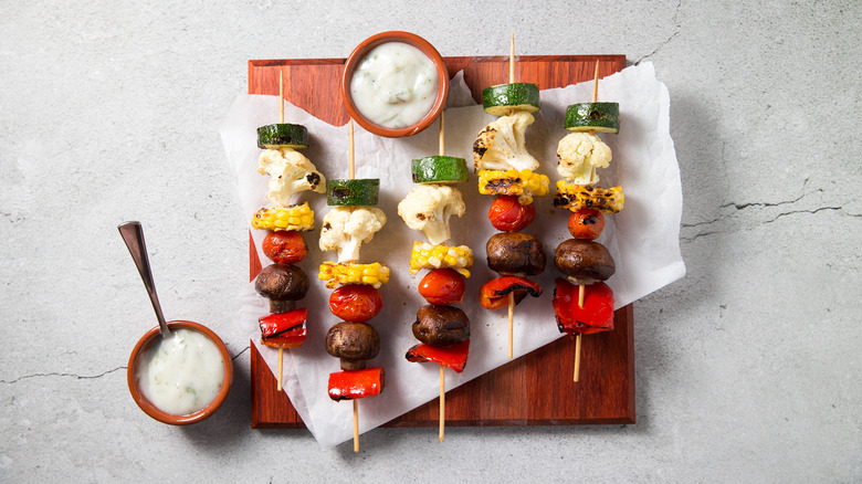 veggie skewers served on wooden board lined with parchment paper next to dipping sauces