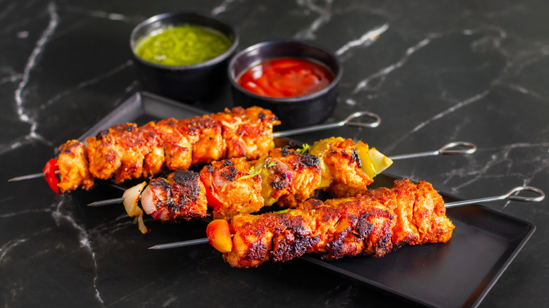 Chicken tikka kebabs on a platter beside ramekins of colorful sauces