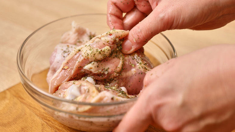 person marinating chicken in a bowl