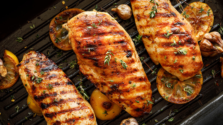 three grilled chicken breasts with lemon slices, garlic, and herbs