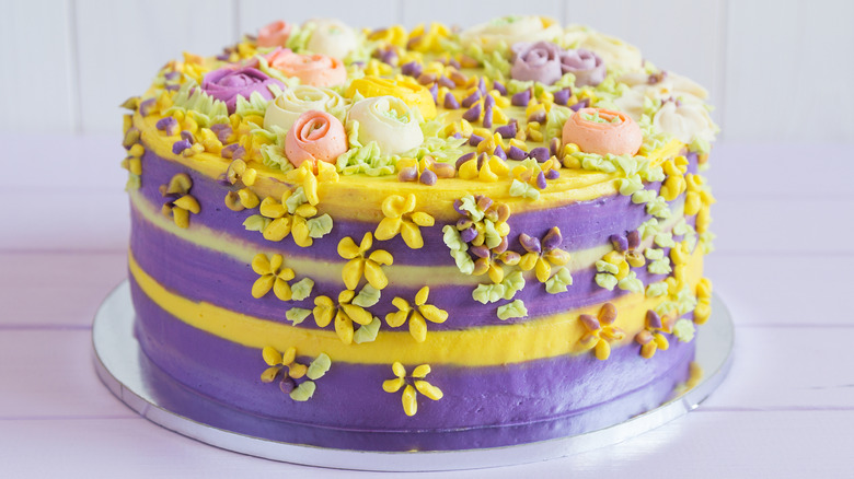 A neatly decorated spring-themed cake with yellow and purple color palette and piped flowers.