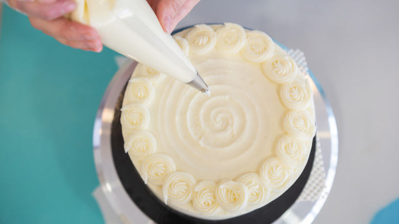 Hands piping vanilla buttercream onto a round cake.
