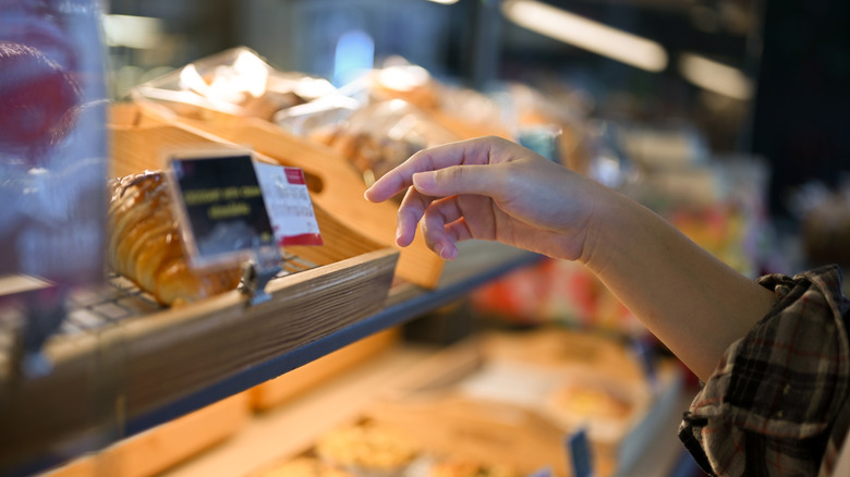 Woman reaches into case to grab pastry with bare hand