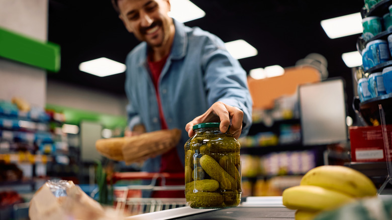 Blurred man in background putting jar of pickles down at the cash register