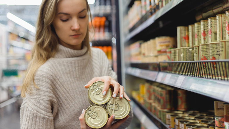 Customer picking up three cans off of a supermarket shelf