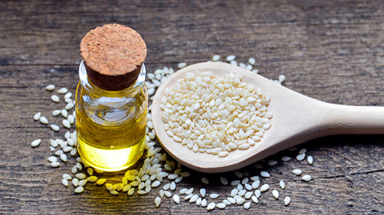 A tiny bottle of oil next to a wooden spoon full of sesame seeds