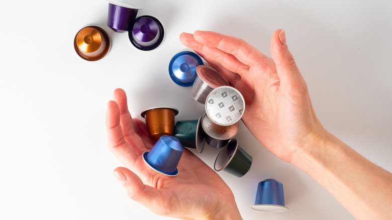 Hands are shown releasing varied Nespresso pods onto white background.