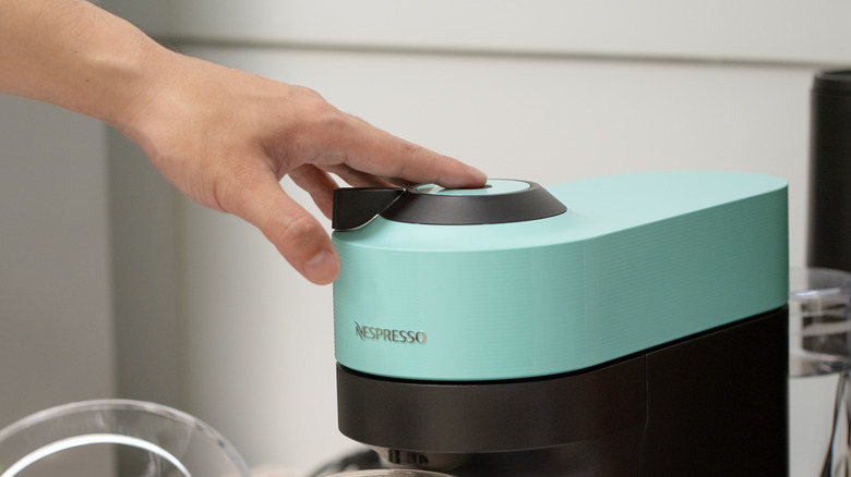 A person presses on the top of a blue Nespresso machine.